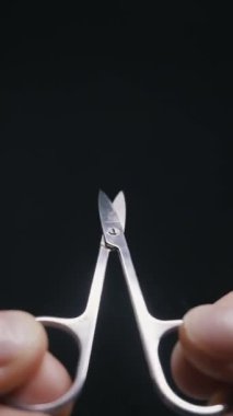 Bir insanın elleri siyah arka planda küçük gümüş bir tırnak makasını açıp kapatır. Kişisel bakım, kişisel bakım, hijyen, hassasiyet ve güzellik tedavileri kavramı.