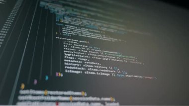 Bilgisayar monitörü, koyu bir arayüzde renkli yazılım programlama kodlarının kaydırma çizgilerini görüntüler. Vibe Kodlama kavramı, yapay zeka yardımı ve modern dijital iş akışı.