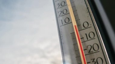 Bir pencereye bağlı açık hava termometresi, bulutlar mavi gökyüzünde hızla hareket ederken dondurucu sıcaklıkları gösterir. Kış hava tahmini, soğuk mevsim atmosferi ve meteoroloji kavramı.