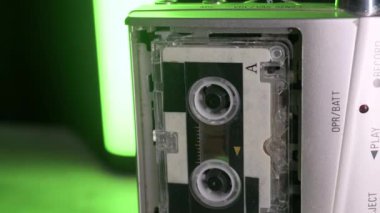 Eski bir gümüş mikrokaset kaydedicisi renkli ışıklara karşı dönen makaralı bir kaset çalar. Retro teknoloji, gazetecilik, analog ses kaydı ve araştırmacı gazetecilik kavramı.