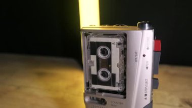 Renkli LED ışıklar arka planda kayarken gümüş renkli bir mikro kaset kaydedici bir kaset çevirir. Retro teknoloji, gazetecilik, araştırmacı gazetecilik ve klasik ses donanımı kavramı.