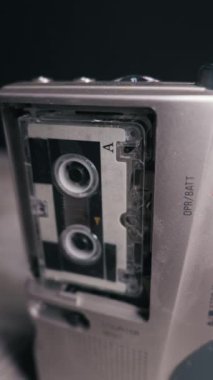 Gümüş renkli bir mikro kaset kaydedici, kayıt sırasında karanlık bir arkaplana karşı dönen kasetçalar ile çalışır. Retro gazetecilik, dikte etme, casusluk ve analog ses teknolojisi kavramı.