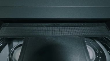 Eller siyah VHS bandını eski video kaset kaydedicinin içine sokuyor. Mekanik yükleme sistemi tahta masa yüzeyindeki ortamı kabul ediyor.