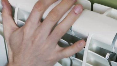 A man's hand checks the temperature of a white central heating radiator in a room. Concept of home comfort, utility bills, energy crisis, and the cold winter season.