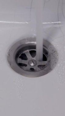 Kapanmadan önce beyaz seramik lavabonun içindeki paslanmaz çelik süzgece temiz bir su akıntısı dökülür. Konsept günlük hijyen ve tesisat işlevselliğini gösteriyor..