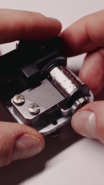 Parmaklar mekanik bir müzik kutusunu tutarken çivilenmiş silindir döner ve metal tarak dişlerini koparır. Müzikal oyuncak mekanizmasının karmaşık hareketlerini vurgulayan bir makro görünüm.