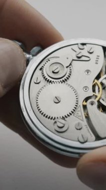 Bir el, karmaşık vitesleri ve salınan dengeyi yakından gösteren açık bir mekanik cep saatini tutuyor. Hassas mekanik ve zaman yönetimi kavramı.