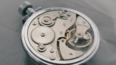 Makro çekim, beyaz duman içinde dönen klasik bir kronometrenin karmaşık iç dişlilerini ve denge çarkını ortaya çıkarır. Mekanik hareket sorunsuz çalışıyor. Hassasiyet kavramı.