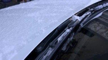 Donmuş arabanın ön cam sileceği kalın kar ve buzla kaplı cama dayanır. Bu kavram, dondurucu hava koşullarında araç bakımında yaşanan zorlukları gösteriyor.