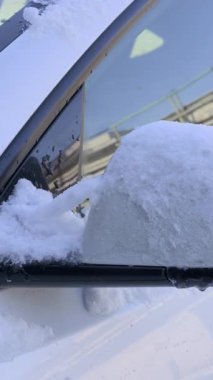 Beyaz bir araç yan aynası yoğun karla kaplı ve fırtına sırasında buz asılı durur. Tehlikeli sürüş koşulları, dondurucu hava ve kış arabası bakımı kavramı.
