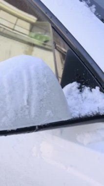 Yakın plan çekimde kar ve buzdan oluşan kalın bir tabaka altında gömülü beyaz bir araba aynası ortaya çıkıyor. Tehlikeli sürüş koşulları, kış bakımı ve dondurucu soğuk kavramı