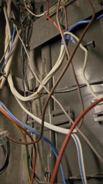 Renkli elektrik kabloları gri metal bir şasinin içindeki beyaz bir terminal bloğunun etrafında dolanır. Kamera, düzensiz devre ve kablo bağlantılarını yavaşça indirir..