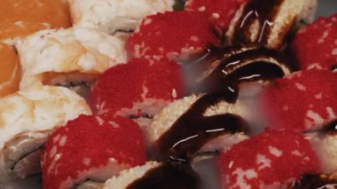 Kırmızı tobiko havyarı ve unagi soslu lezzetli bir suşi setinin makro dönüşümlü çekimi. Gurme tabağından bir ışık buharı yükseliyor. Japon mutfağı, güzel yemekler ve taze deniz ürünleri kavramı..