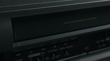 Bir el eski, siyah bir VCR oynatıcının yuvasına bir video kaset yerleştirir. Makine kaseti mekanik olarak yüklüyor. Nostalji kavramı, 80 'lerin medyası ve klasik teknoloji..