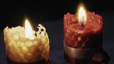 Bal peteği desenli iki balmumu mum yansıtıcı yüzeyde parlak bir şekilde yanarken kamera uzaklaşıyor. Romantik atmosfer kavramı, ruhsal rahatlama ve sıcak tatil gelenekleri..