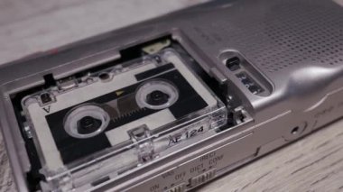 Yakından bakıldığında, ahşap bir yüzeyde duran mikro kaset bantlı gümüş renkli bir diktafon görülüyor. Retro gazetecilik kavramı, analog teknoloji ve seksenlerin nostaljisi..