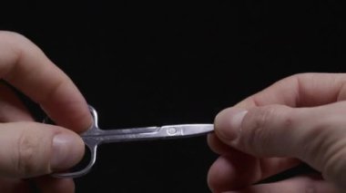 Küçük metal manikür makasını tutan ve manipüle eden birinin ellerinin detaylı görüntüsü. Kişisel bakım, hassasiyet, maharet ve dikkatli kullanım araçları kavramı.