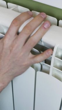 Isıyı kontrol etmek için beyaz bir kalorifere dokunan bir erkek eli. Kişi, merkezi ısıtmanın düzgün çalışıp çalışmadığını kontrol etmek için metal parçalarını hisseder. Ev ısıtma mevsimi kavramı
