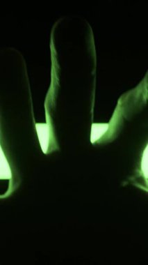 Karanlık, siluetli bir el, karanlıkta parlayan renk değiştiren LED ışık şeridine uzanıyor. Fütürist teknoloji kavramı, biyometrik güvenlik, gizem ve soyut gece hayatı atmosferi