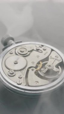 Gümüş mekanik saat hareketini kapat vitesler dönüyor ve beyaz duman içinde salınan denge çarkı. Zaman geçişi, hassas mühendislik ve tarih kavramı.