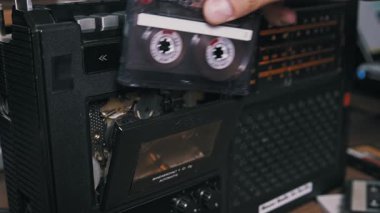 Eski bir teybe eski bir ses kaseti yerleştiren ve çalma tuşuna basan bir elin yakın çekimi. Retro teknoloji kavramı, nostalji, 80 'ler ve 90' ların müzik kültürü ve modası geçmiş medya