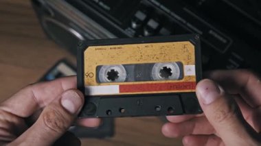 Erkek eller, arka planda bulanık bir teybe karşı yıpranmış sarı bir ses kaseti tutuyor. Seksenlerin müziği, analog teknoloji tarihi ve retro medya biçimleri nostaljisi..