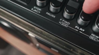Klasik bir kasetçaların çalma tuşuna basan bir parmağın makro görüntüsü. Dokulu siyah tuş ve beyaz etiketler retro ses panelini vurgular.