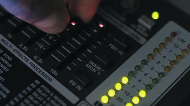 Aydınlatılmış EQ faderlarını dijital çoklu efekt işlemcisine ayarlayan bir ses mühendisinin elinin yakın çekimi. Sarı LED seviyeleri karanlık, profesyonel kayıt stüdyosunda aktiftir.