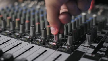 Profesyonel bir ses karıştırma konsolunun kontrol düğmelerini ayarlayan bir eli kapat. Bu konsept ses mühendisliğini ve ses kalibrasyonunu bir stüdyoda gösterir..
