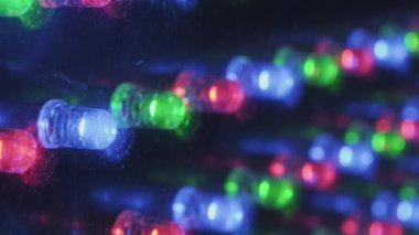 Açılı makro çekim bir panelde yanıp sönen RGB LED ışıkları yakalıyor. Sığ alan derinliği ön plandaki diyotlara odaklanarak karanlık bir ortamda dinamik renkli bir bokeh etkisi yaratır..