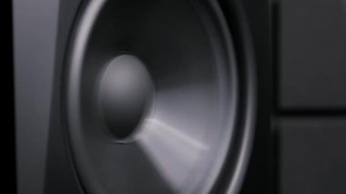 Güçlü ses dalgaları oluştururken yavaşça titreşen siyah bir hoparlörün yakın çekimi. Dinamik sürücü bir müzik stüdyosunda ritmik düşük frekanslı titreşimler yaratır..