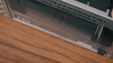 Eski bir stereo desteyi açan ve eski bir kaseti kaldıran bir elin makro görüntüsü. El sarı etiketli bandı çıkarır ve gümüş oyuncunun kapısını kapatır..