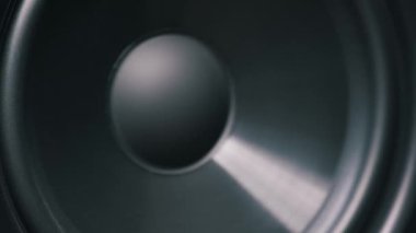 Düşük frekanslı bas ritmiyle titreşen siyah bir woofer membranın ön görüntüsü. Hoparlör sürücüsü sorunsuzca girip çıkıyor, stüdyoda derin ses titreşimleri yaratıyor..
