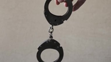 Arka planda metal bir kelepçe tutan bir elin yakın çekimi. Çelik kelepçeler zincir ve kilit mekanizmasını göstermek için sallanır ve döner..