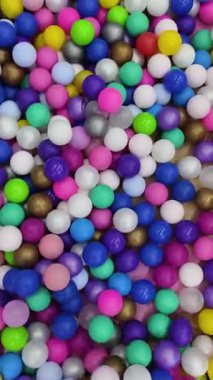 Canlı, renkli plastik topların sallanışının yukarıdan aşağı görüntüsü. Pembe, mavi, yeşil, mor, sarı ve altın küreler rastgele hareket ederek bir çocuk oyun alanından soyut bir doku oluştururlar..