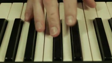 Erkek eller dijital piyano klavyesinde akor ve melodi çalar. Yakın çekim, değişken mor, mavi ve yeşil neon ışıklarla aydınlatılmış..