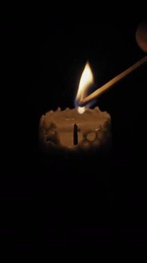 Bir el, zifiri karanlık bir zemine balmumu fitilini tutuşturmak için yanan kibrit kullanır. Umut kavramı, ruhani dua, romantik atmosfer ve sıcak kış akşamları..