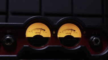 Ses arayüzündeki ses seviyelerini ölçen iğnelerle arkadan ışıklandırılmış analog VU ölçümlerinin yakın çekimi. Ses mühendisliği, müzik üretimi ve hassas ses ölçümü kavramı.