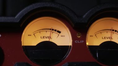 İki kehribar ışıklı analog VU metreye yakın çekim. Ses sinyalini ölçmek için iğneler dalgalanıyor. Ses mühendisliği, müzik üretimi, yayın ve ses kontrolü kavramı.