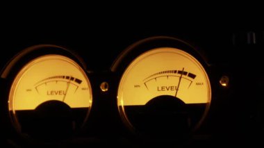 Ses seviyelerini ölçmek için hareket eden iğnelerle arkadan aydınlatılmış iki adet analog VU metreye yakın çekim. Klasik ses teknolojisi, müzik üretimi ve kesinlik ölçümü kavramı.