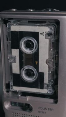 Klasik bir gümüş mikrokaset kaydedicisi yakın plan dikey çekimde dönen makaralı bir kaset çalar. Geçmişe dönük teknoloji, gazetecilik, araştırmacı gazetecilik ve 90 'ların nostaljisi..