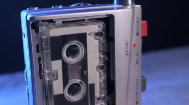 Gümüş renkli bir mikro kaset kaydedicisi, kamera değişen ışığa doğru yaklaşırken dönen makaralı bir kaset çalar. Retro teknoloji, gazetecilik, izleme ve nostaljik elektronik kavramı.