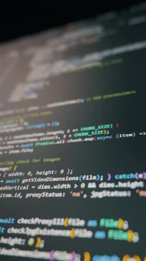 Bilgisayar kodları, keskin makro odaklı ve bulanık kenarlı karanlık bir monitör ekranında kayar. Yazılım geliştirme, veri işleme ve modern siber güvenlik teknolojisi kavramı.