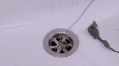 Bir insan, ince metal tel bir aletle büyük bir küme kirli saç ve kir çıkararak tıkanmış banyo lavabosunu temizler. Rutin bakım ve tesisat hijyeni kavramı.