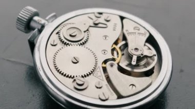 Açığa çıkmış iç dişlilerin dönüşümlü görüntüsü ve klasik gümüş bir cep saatinin denge çarkı. Mekanik hareket, hassas mühendislik ve klasik zaman tutma kavramlarını gösterir..