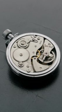 Açık sırt çantalı klasik gümüş kronometre, çalışan vitesleri ve salınan denge çarkını siyah yüzeyde gösteriyor. Hassas mühendislik ve mekanik zaman tutma kavramını vurgula.