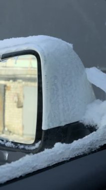 Kalın kar ve buzla kaplı beyaz araba aynası. Kenarlarından sarkık buz sarkıyor. Cam dışarıdaki tuğladan bir garaj duvarını yansıtıyor. Kavram tehlikeli kış sürüş koşullarını göstermektedir
