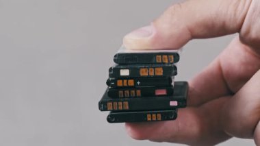 Gri arka planda kullanılmış bir yığın cep telefonu pilini tutan bir elin yan görüntüsü. Elektronik atık imhası ve çevresel etkiye odaklan.