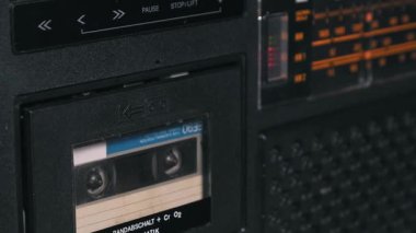 Mavi etiketli bir kaseti kaldırmak için retro siyah boombox 'ın fırlatma tuşuna basan bir elin yakın plan görüntüsü. Boş bant destesinin kapatılması eski teknolojinin iç mekanizmasını vurgular.