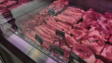 Pirzola ve fileto gibi çeşitli çiğ domuz pirzolaları soğutulmuş bir vitrinde güzelce düzenlenir. Kiril metni ve pembe ışıklandırmalı siyah fiyat etiketleri tipik bir kasap dükkanı atmosferi yaratıyor.